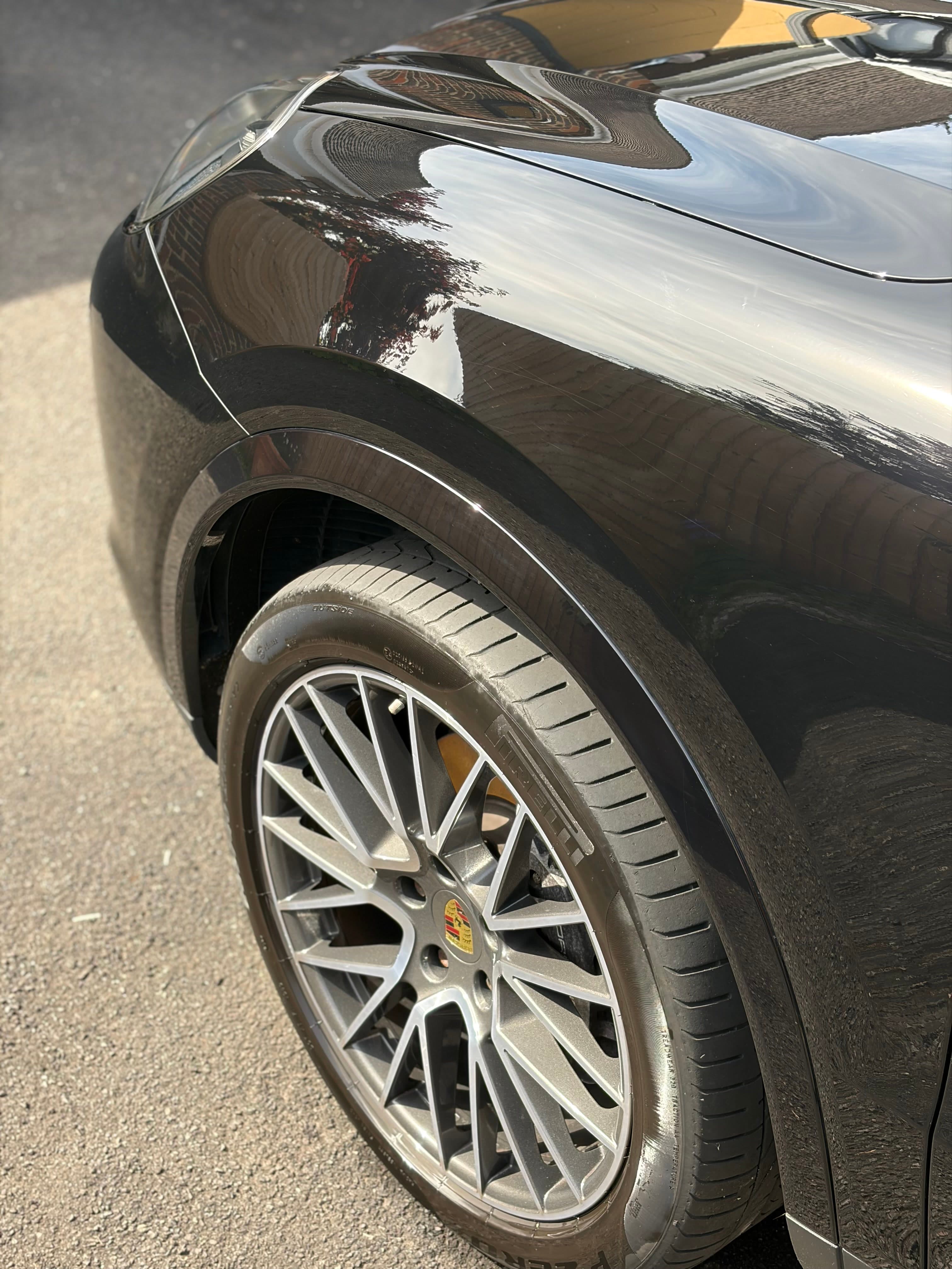 Sunlit detailed front wheel and glossy arch of a black Porsche Cayenne after a full valet